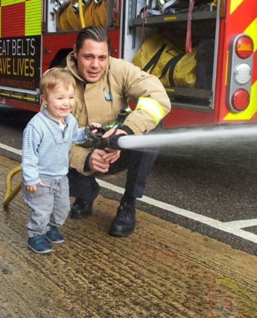 Firefighter Adam sprays firehose with child looking on