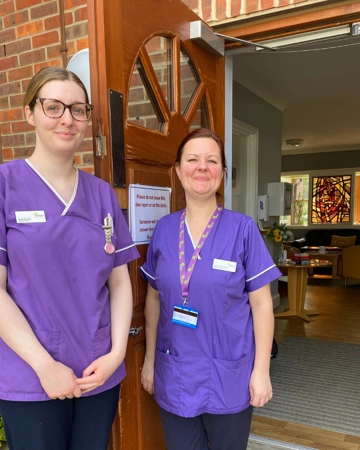 Two healthcare assistants hold the door open for a patient