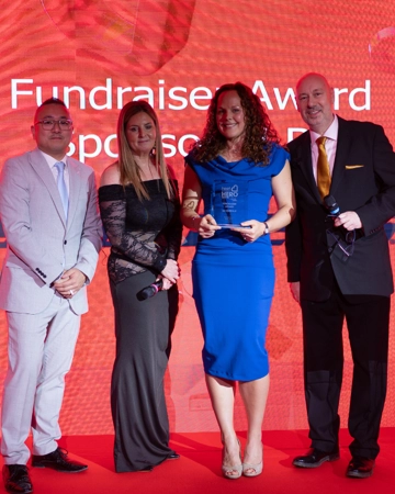 Fundraiser in blue dress holds Heart Hertfordshire Hero award
